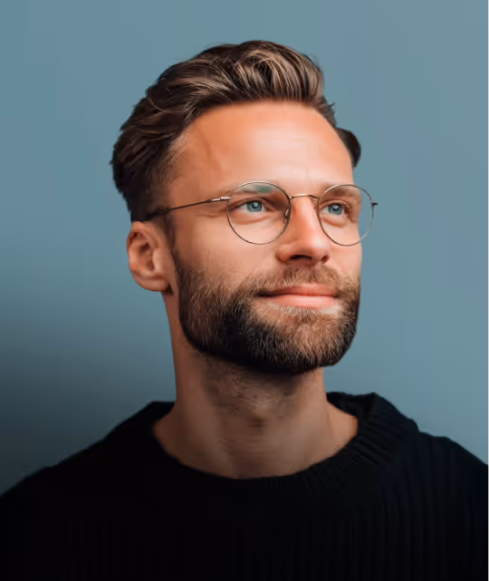 Mężczyzna z brodą, krótkimi włosami i okrągłymi okularami patrzący w prawo na niebieskim tle.