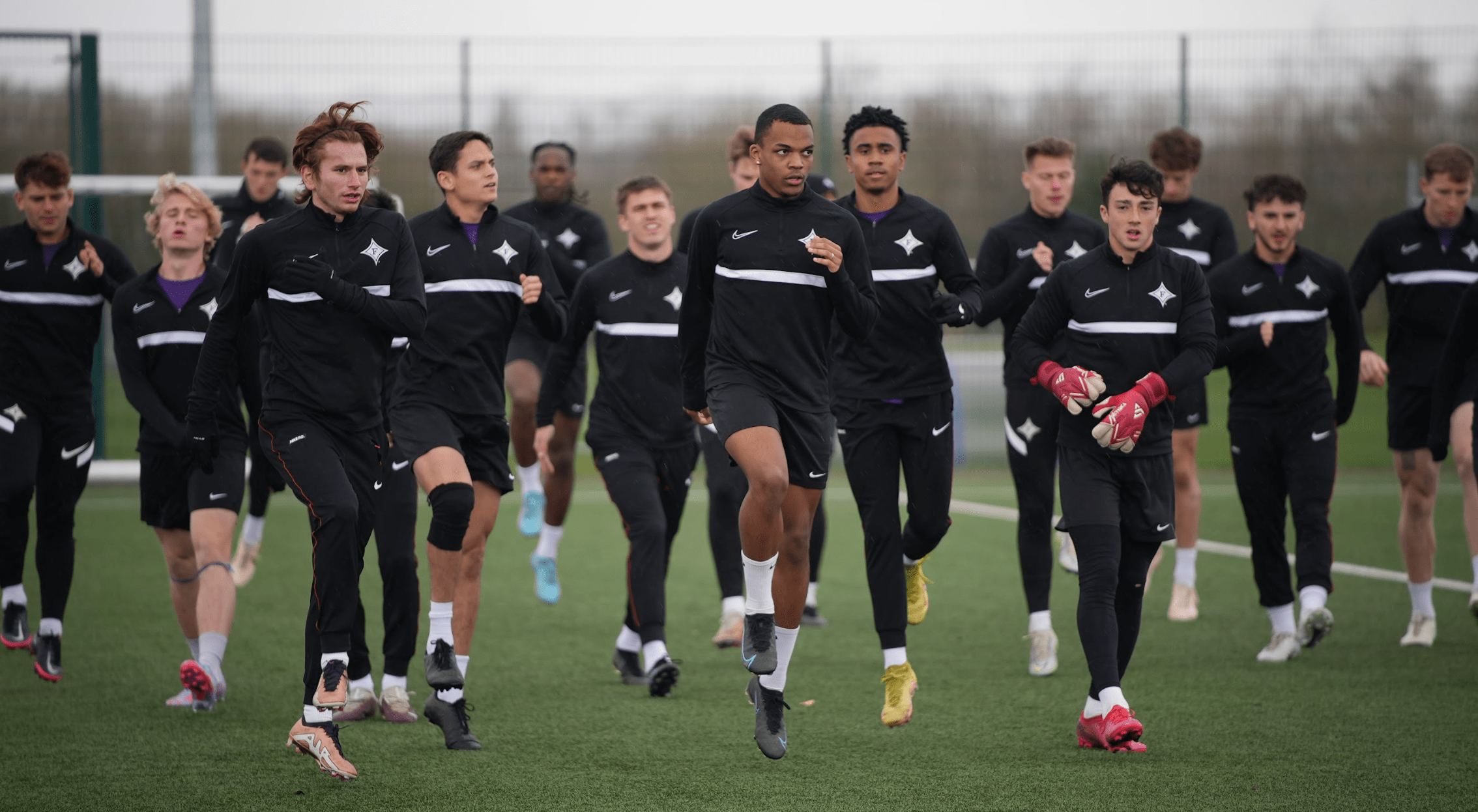 Female wearing a green cardigan smiling into the distance sat next to a male in a white tshirt smiling into the distance at someone on the other side of the desk.