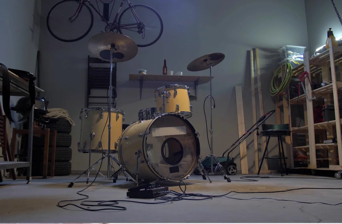 Yellow drum set with cymbals in a garage with tools, tires, and a bicycle on the wall.