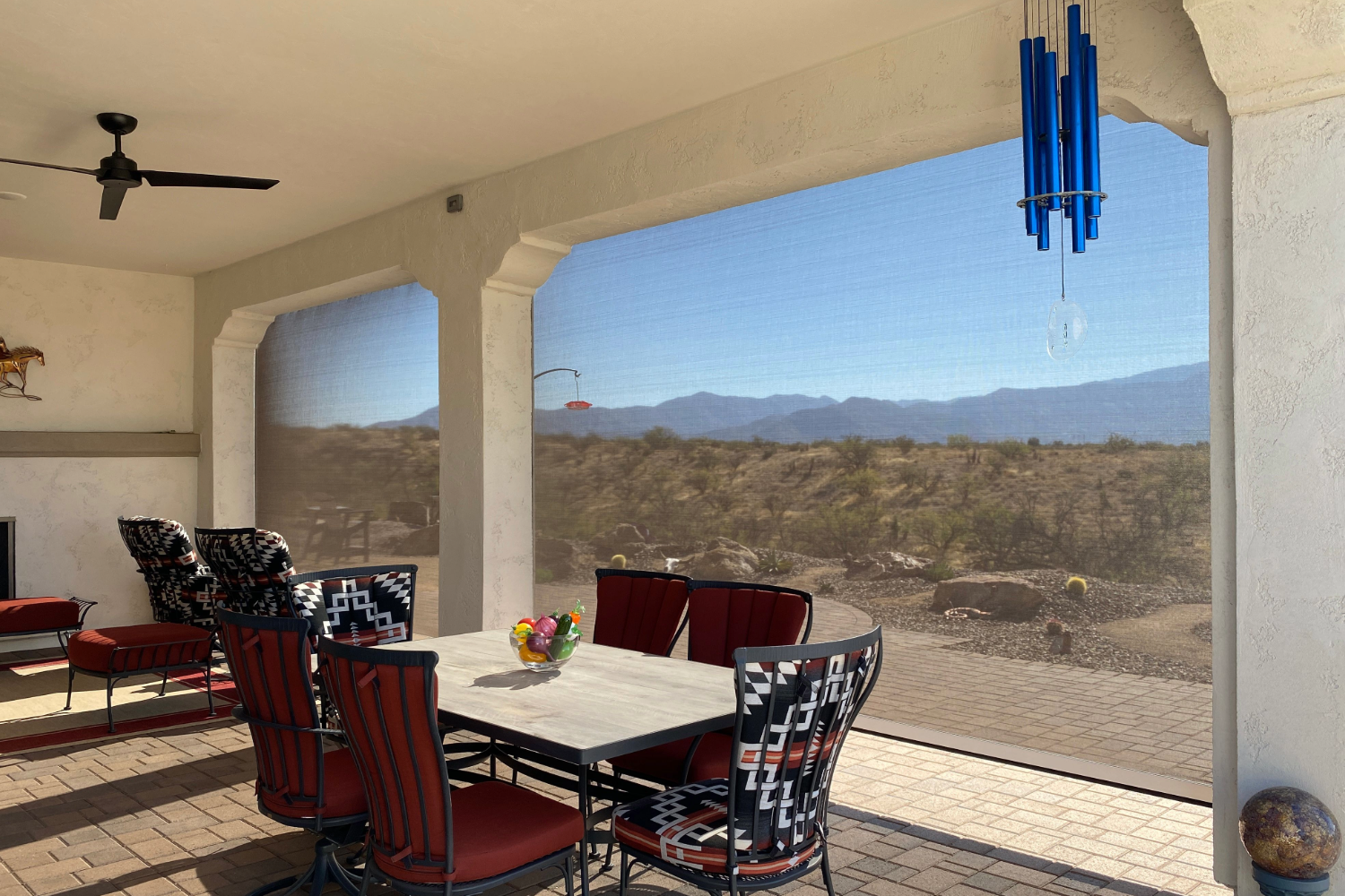 Outdoor patio with screen, table, and red chairs overlooking desert landscape.
