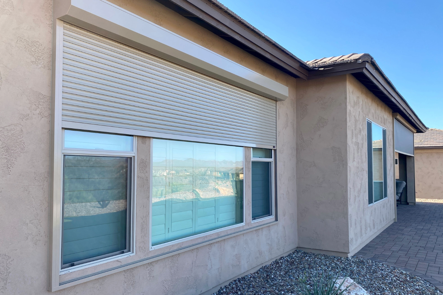 Exterior windows with closed rolling shutters on a beige house.