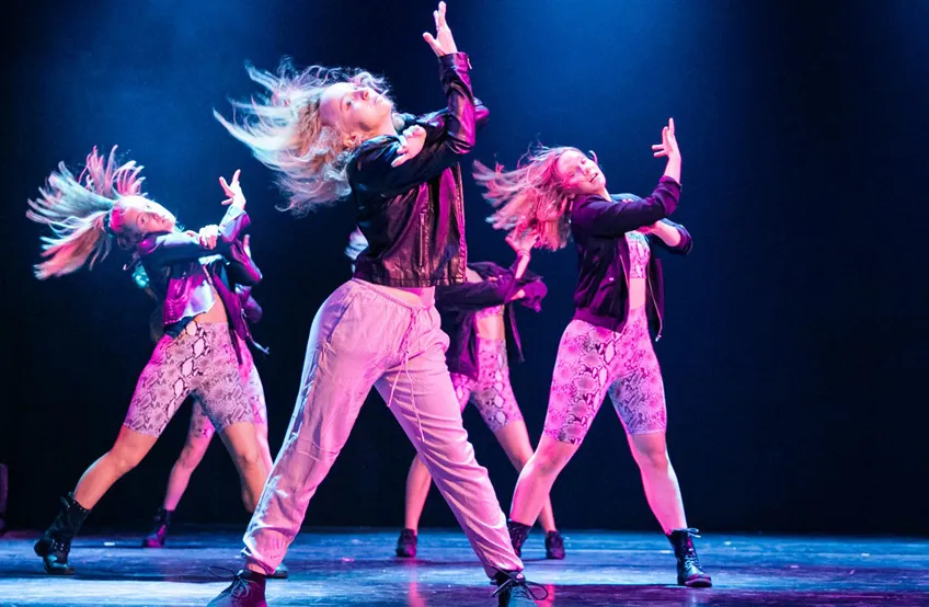 Dansare i rosa och svarta kläder som uppträder energiskt på scenen