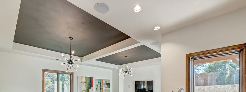 Sophisticated living area with dramatic coffered ceiling featuring gray accents, modern chandeliers, and elevated smoke detector placement.