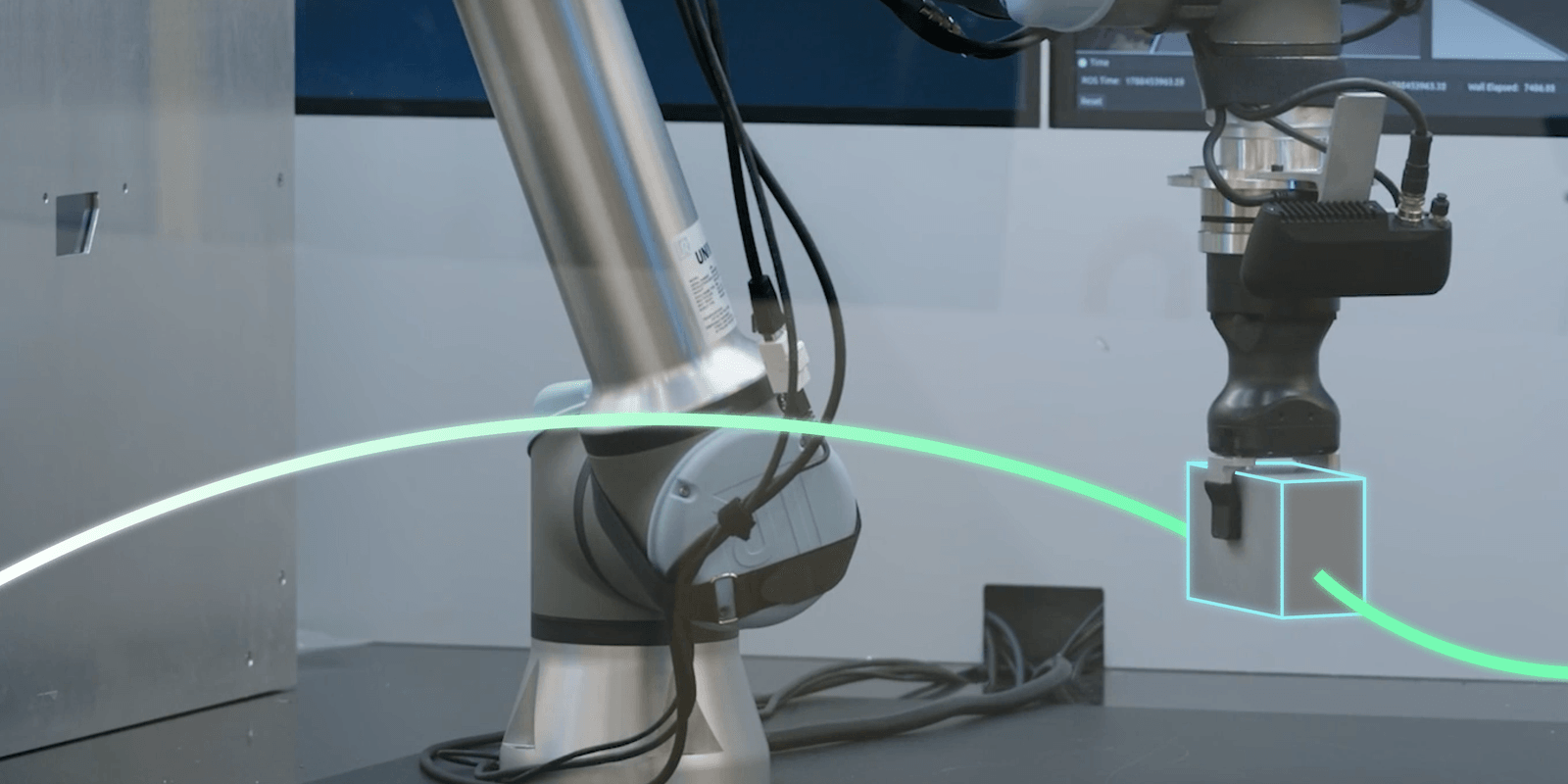 A Universal Robots arm with a gripper holding a metal cube, with a cyan pose-estimation box drawn around the part and a green planned trajectory curving across the frame