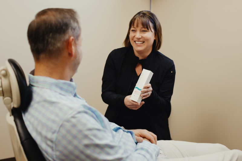 Female dentist in dark clothing discussing treatment with male patient in clinical exam room