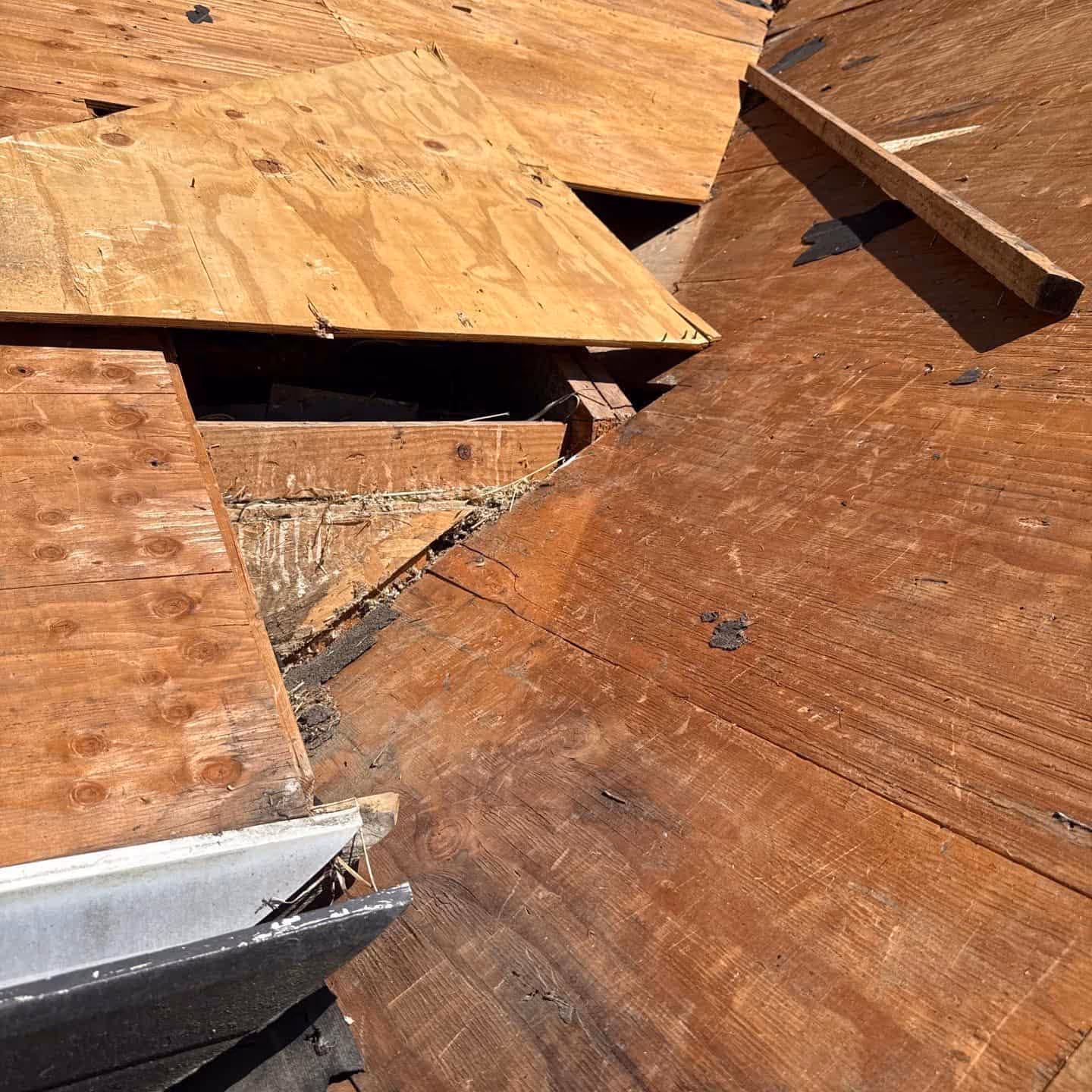 Damaged wooden roof decking with broken and exposed boards showing signs of rot and structural issues, photographed during roof repair.
