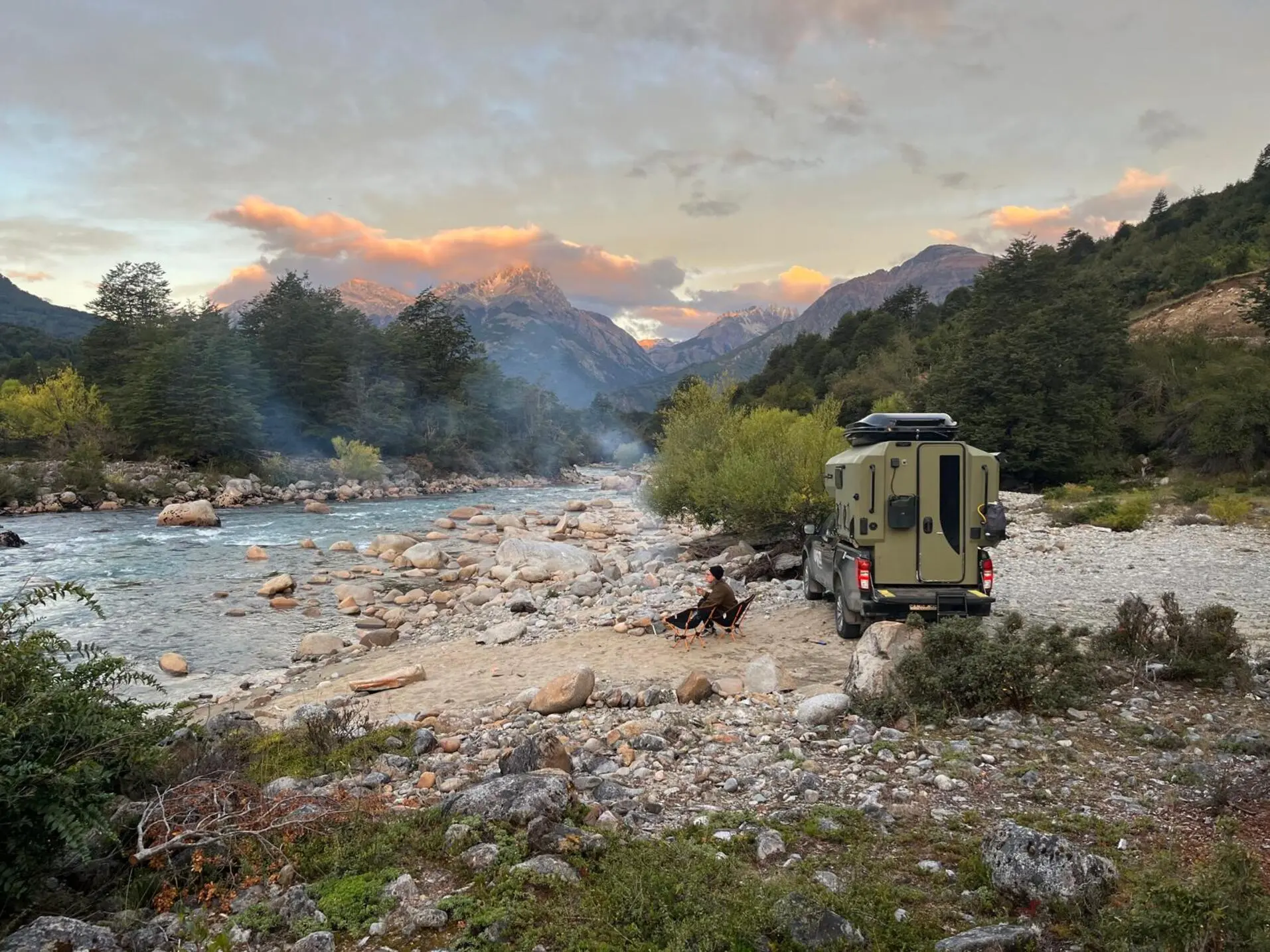 Uozi camper parked beside a rocky river at sunset
