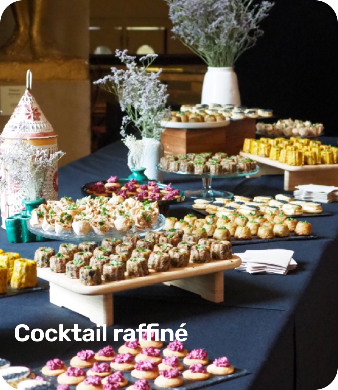 Table with an elegant arrangement of assorted bite-sized appetizers and small desserts on glass and wooden stands with white floral decorations.