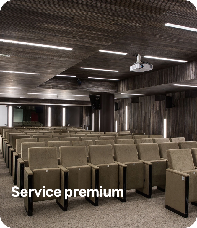 Modern conference room with rows of beige upholstered chairs, dark wood panel ceiling, and a ceiling-mounted projector.