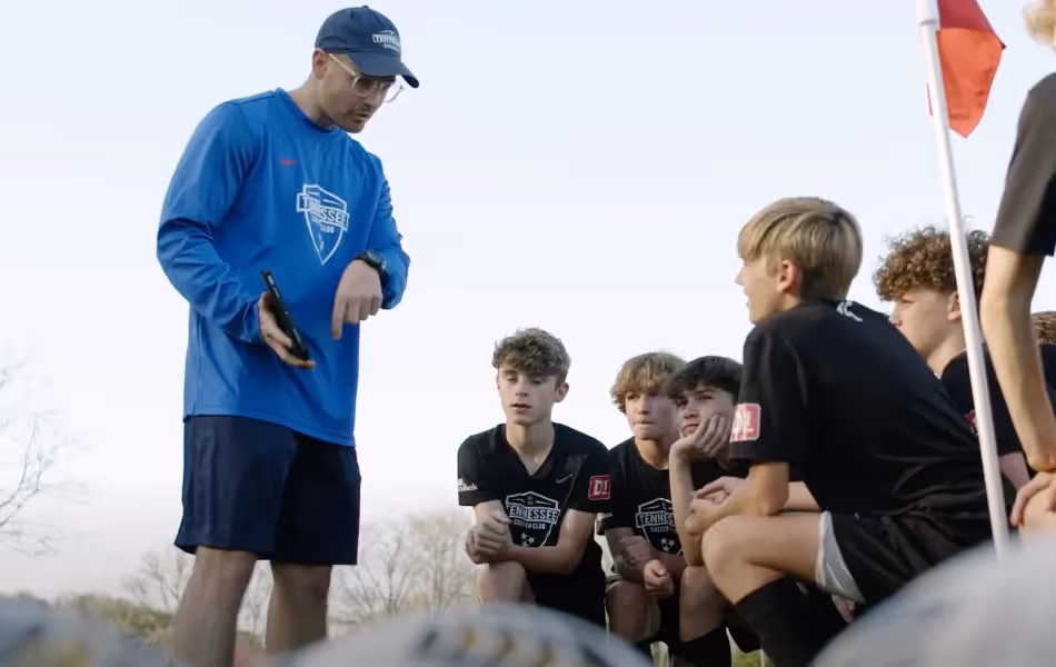 A photo of a coach from a Tennessee soccer club showing his players a video from their previous match recorded by a Veo sport camera, while they stand in a huddle on the soccer field.