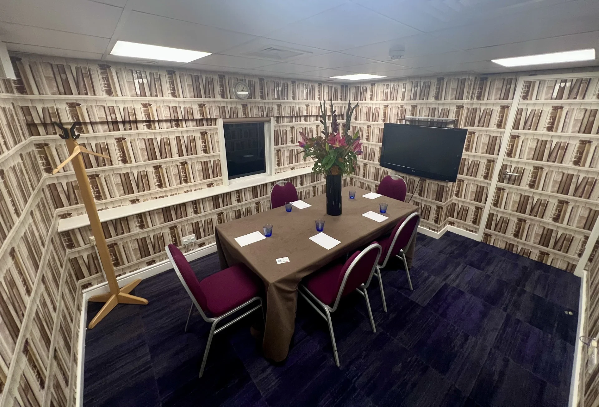 A boardroom at 22 Duchess Mews with bookshelf wallpaper and two wall-mounted screens
