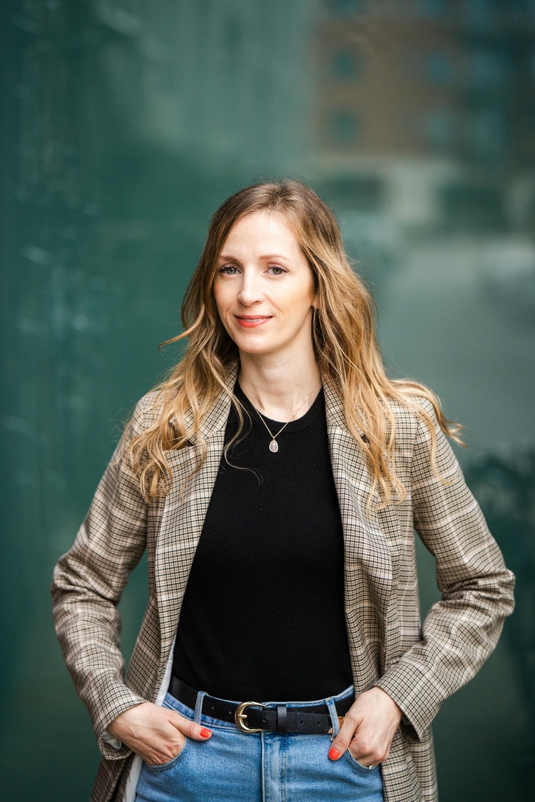 Jeni Miles, founder of WholeLoop Labs and a behavioural scientist and changemaker, stood in front of a green reflective background dresses smartly looking at the camera