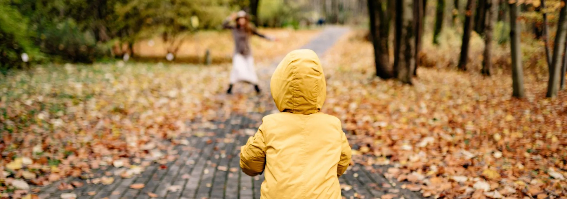A child wearing a yellow raincoat cycling a bike on an autumn day