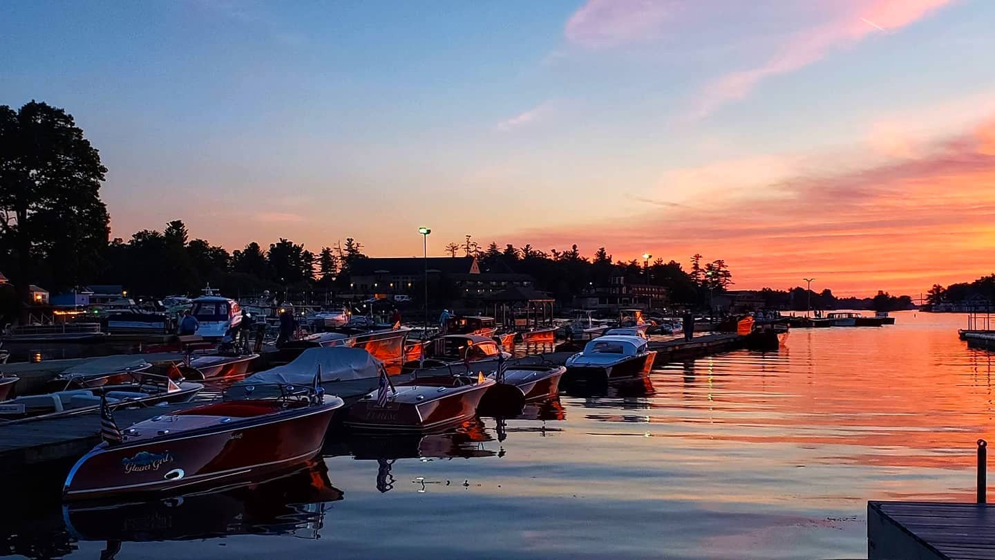 Boats docked at a marina during a colorful sunset with reflections on calm water.