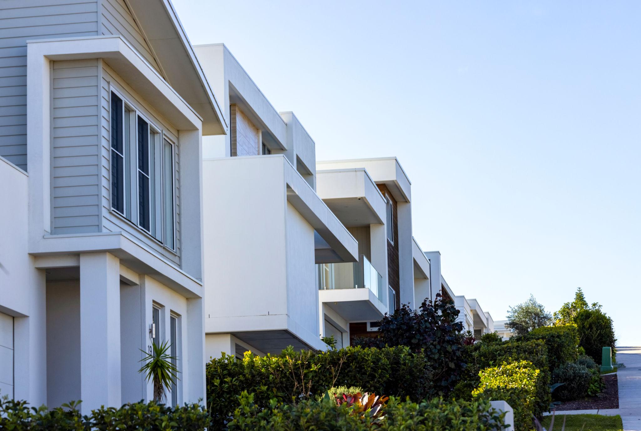 Modern white two-storey townhouses with balconies and garden beds