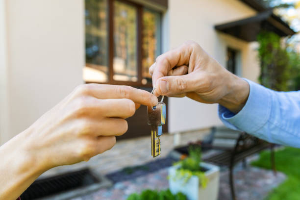 One hand passing house keys to another outside a home