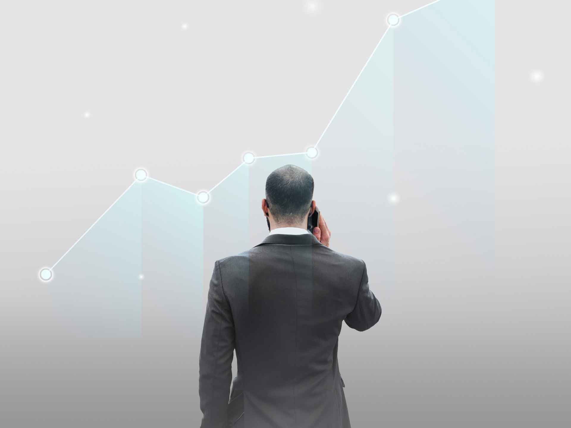 Man on a phone standing in front of a faint rising line graph
