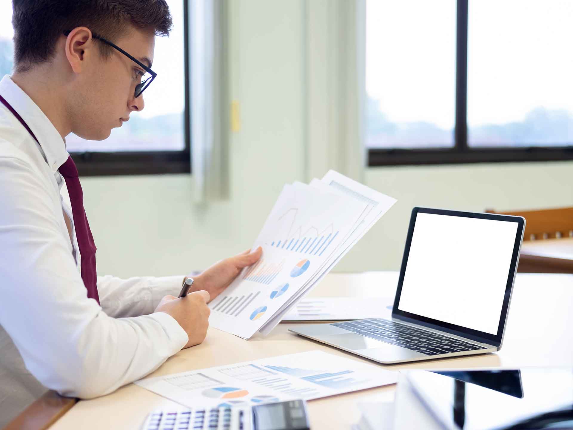 Person at a desk reviewing printed charts beside a laptop