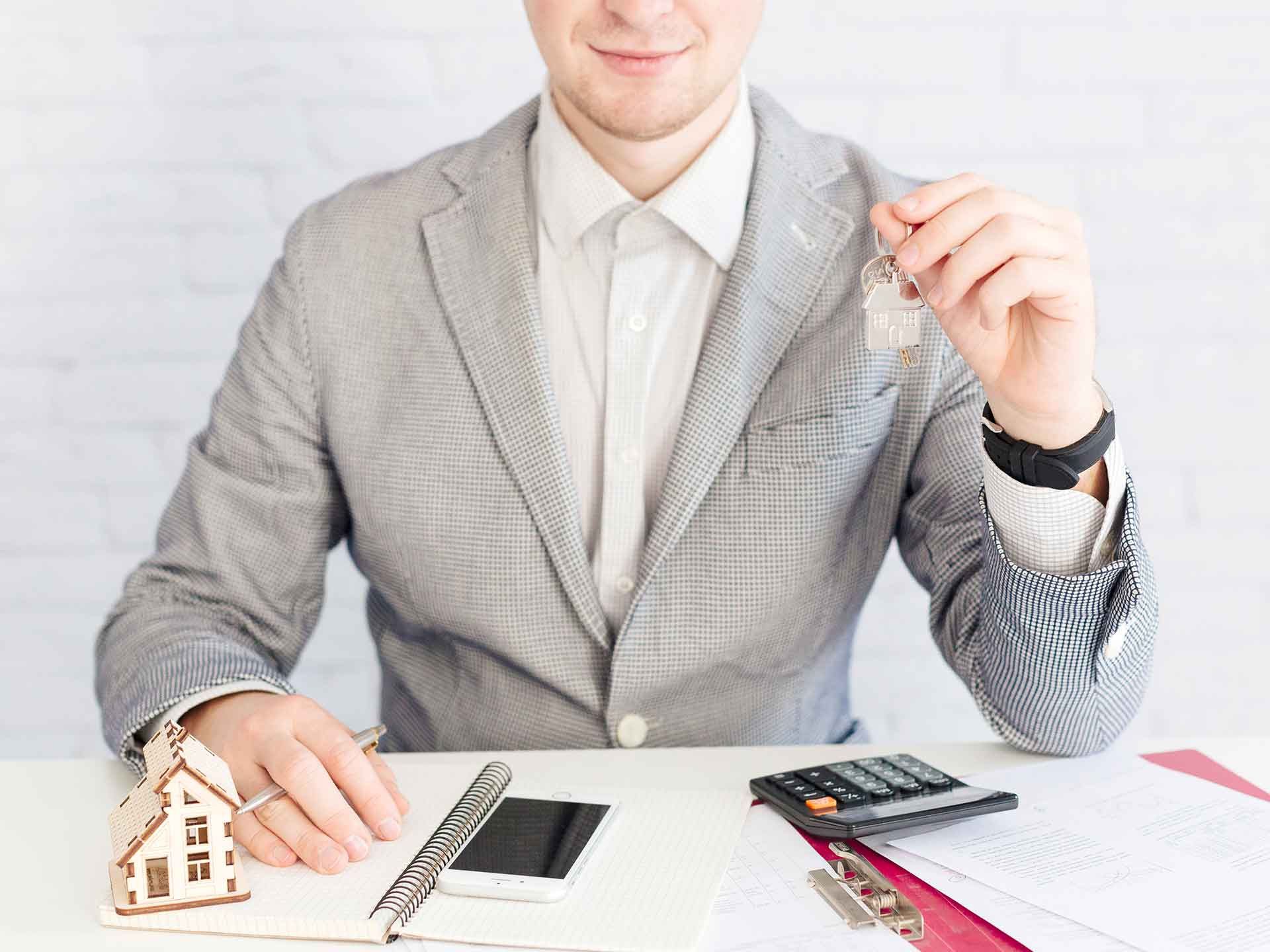 Person at a desk with a model house, calculator and keys
