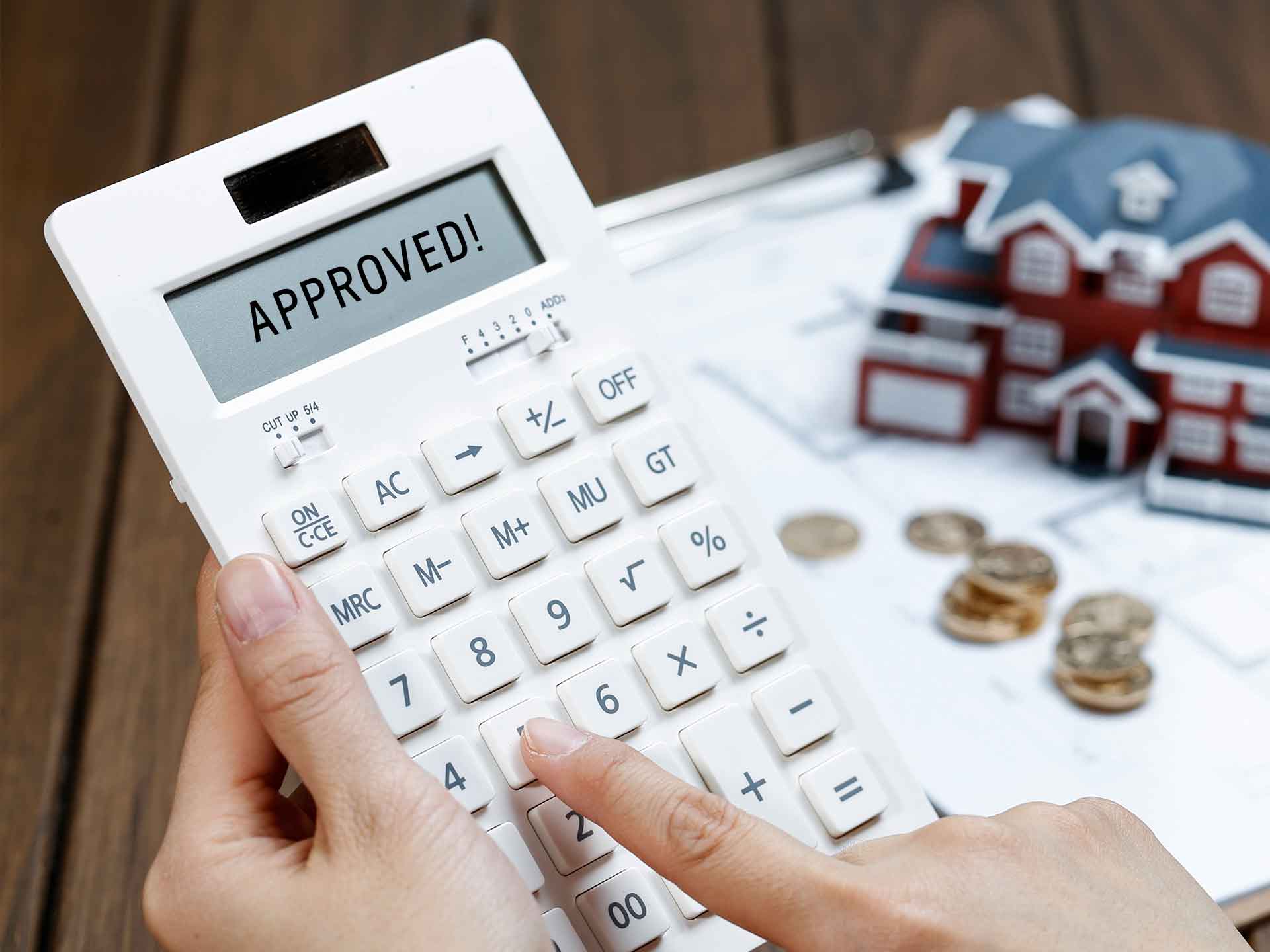 Hand using a calculator displaying 'Approved' beside model houses