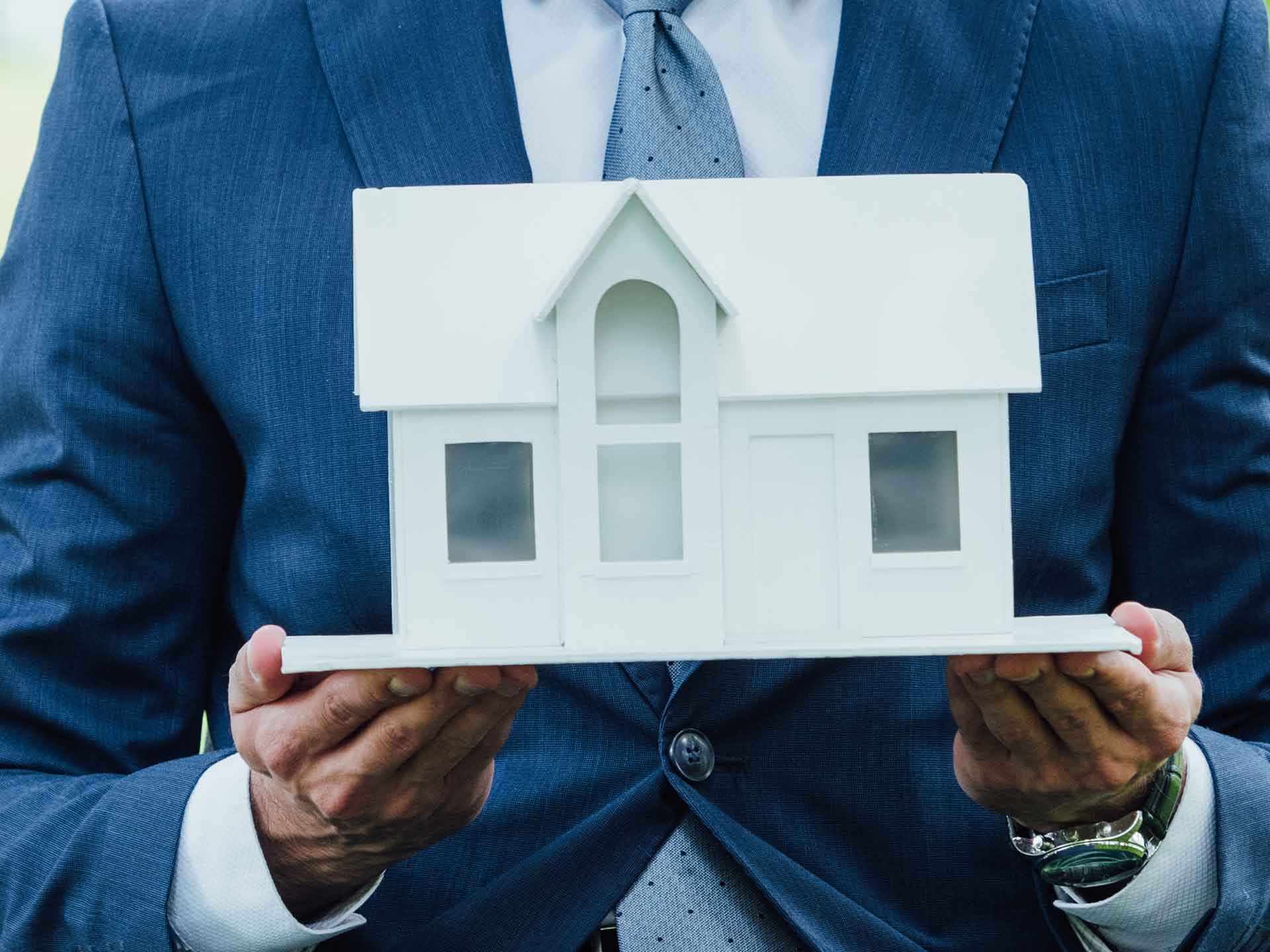 Person in a suit holding a white model house
