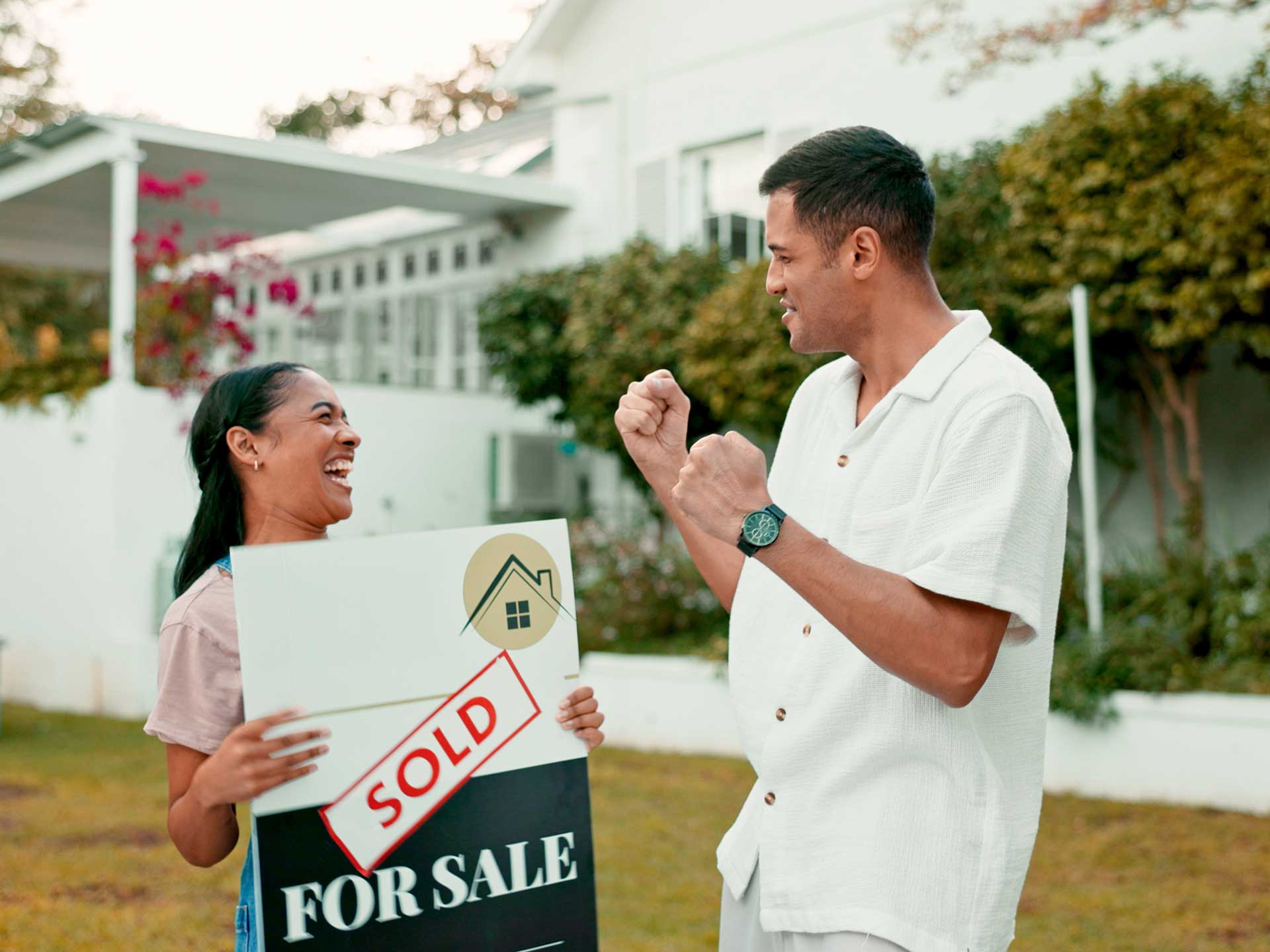 Couple celebrating outside a house holding a 'Sold' sign