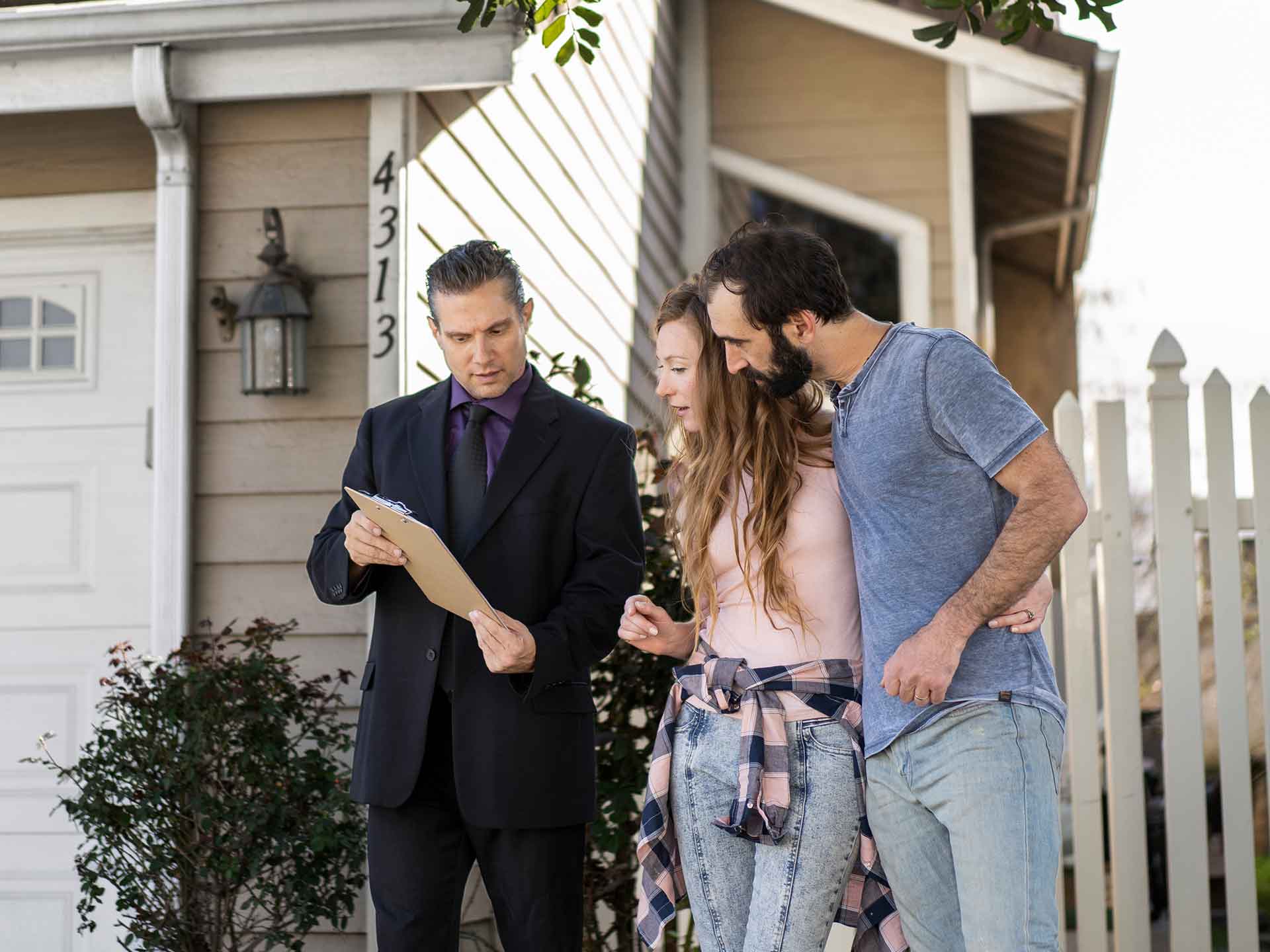 Agent with a clipboard showing a couple a house from the front yard