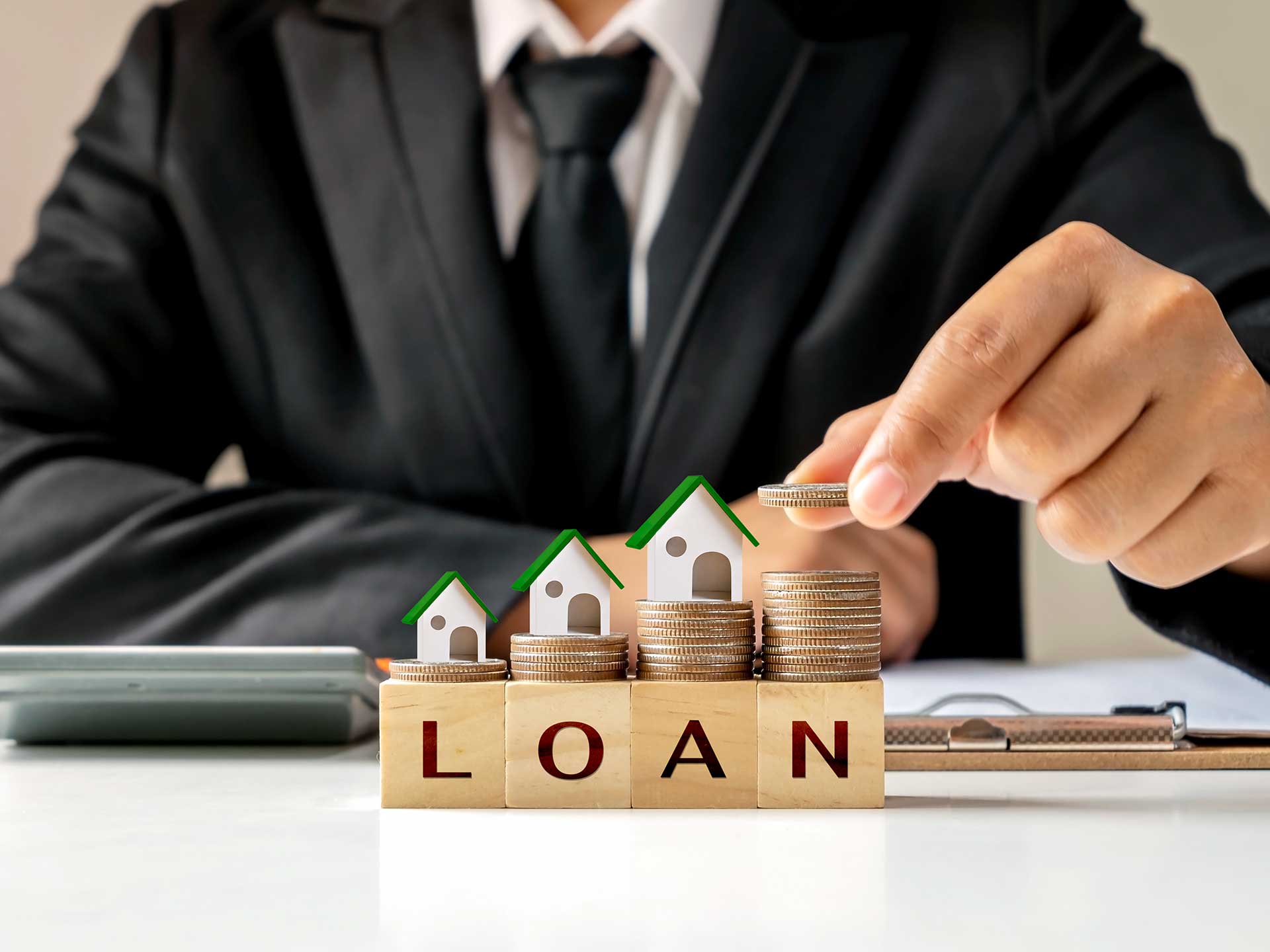Hand placing a coin on wooden blocks spelling 'loan' beside model houses