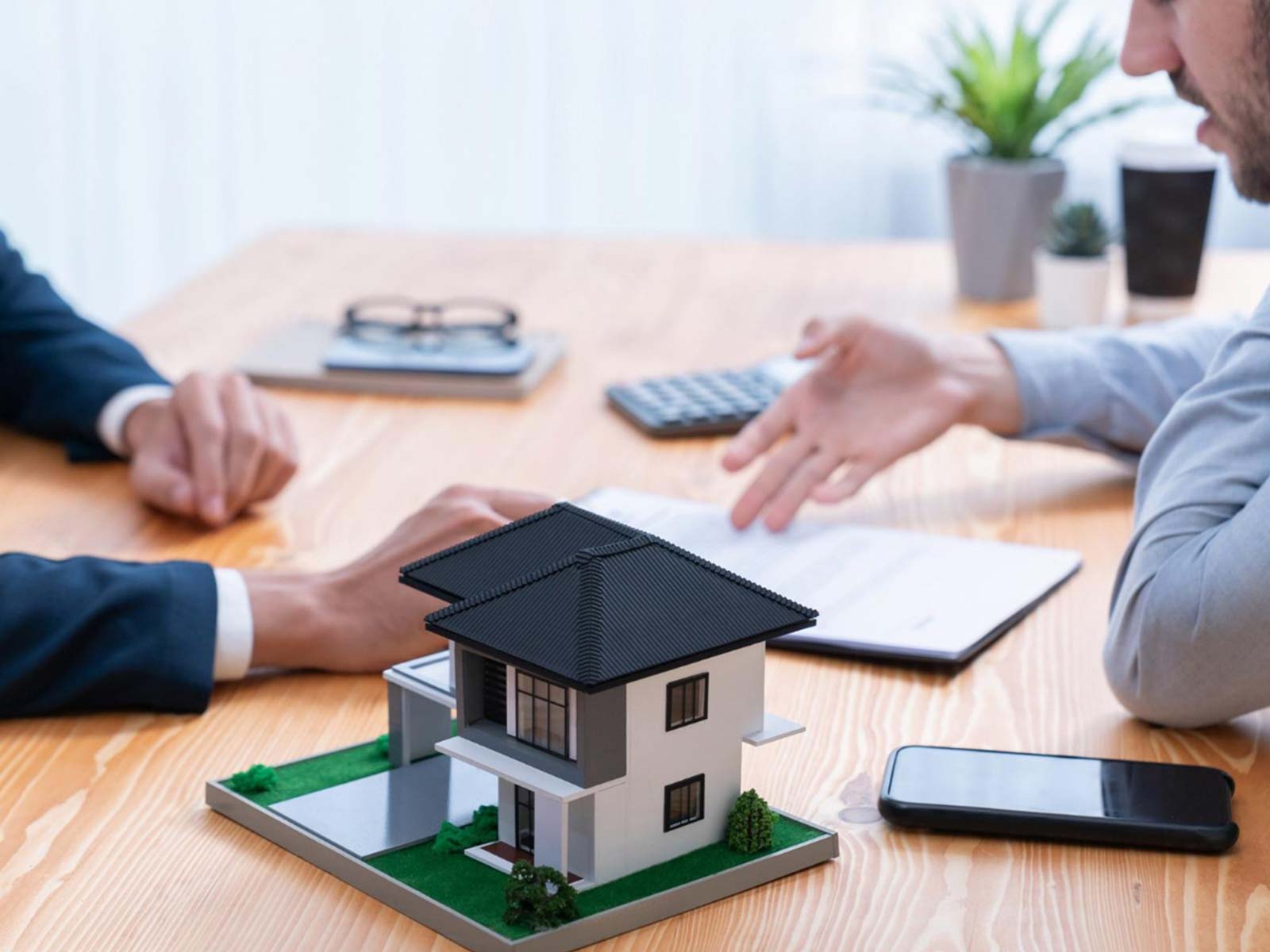 Two people talking across a desk with a model house and calculator