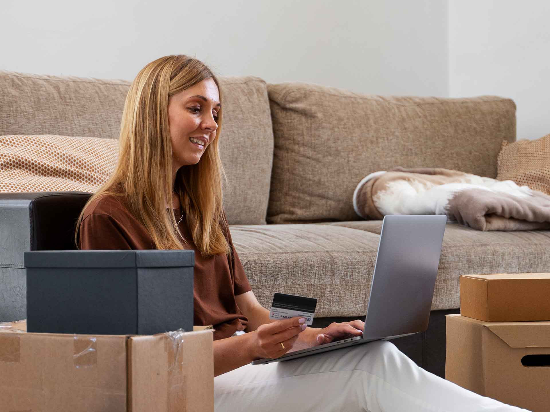 Woman with a laptop on a sofa surrounded by moving boxes