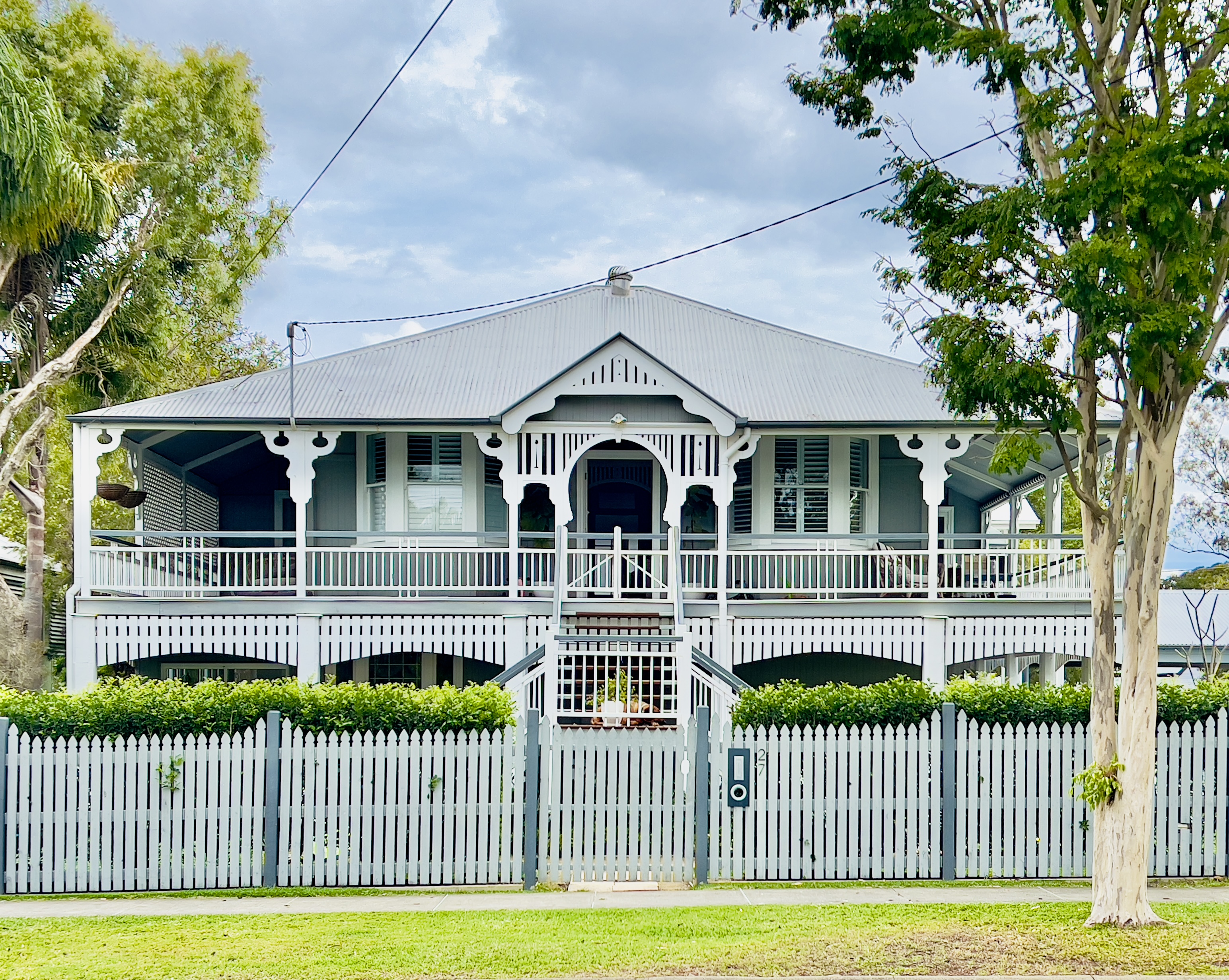 Traditional Queenslander weatherboard house behind a white picket fence