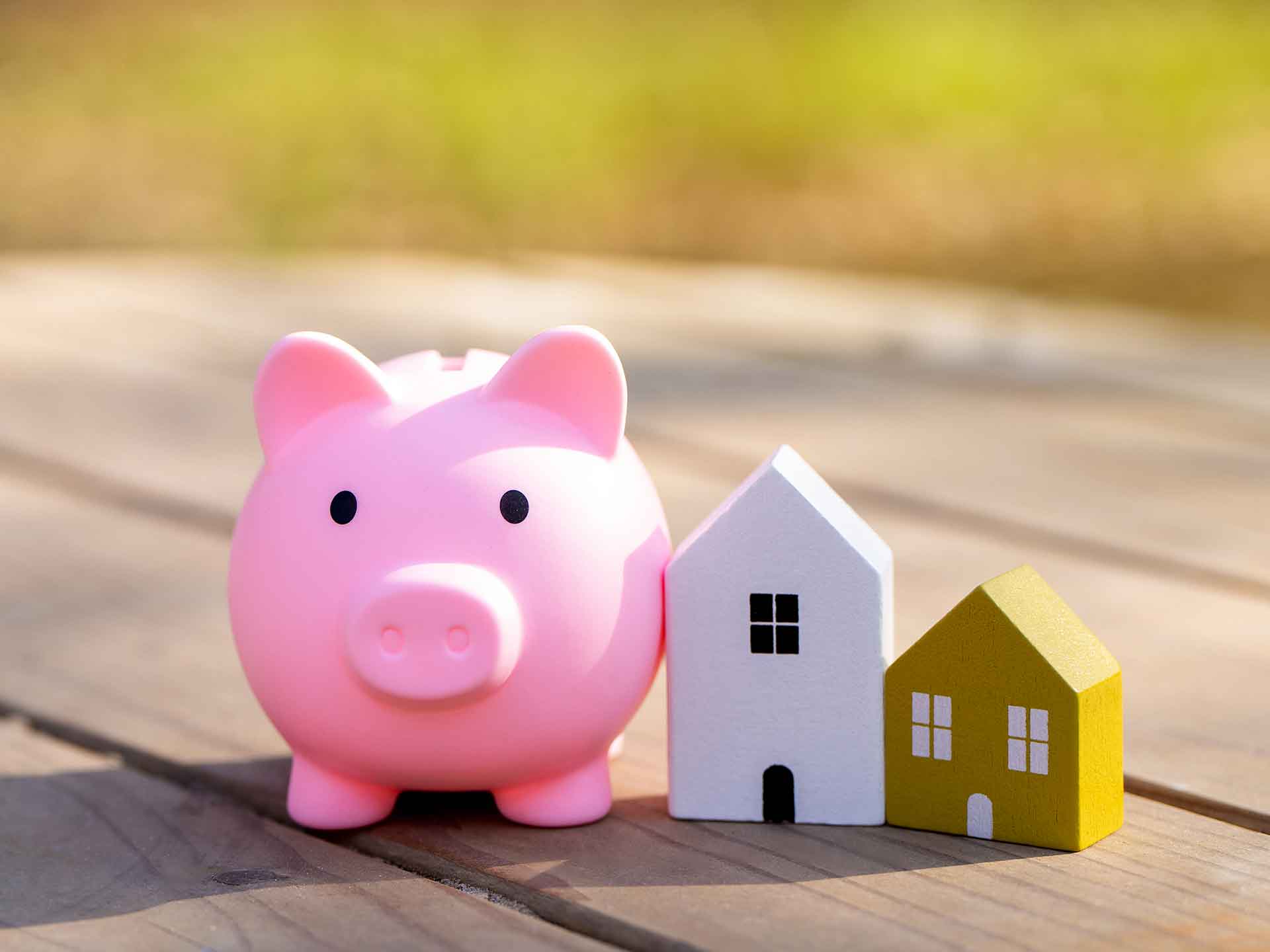 Pink piggy bank beside small white and yellow model houses