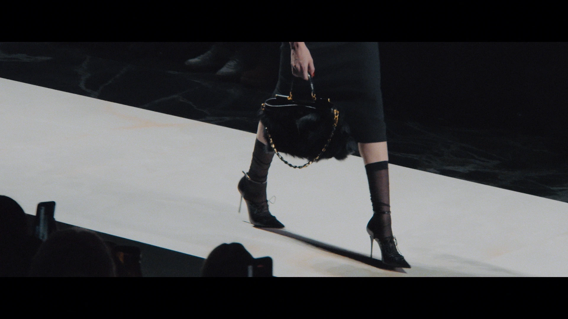 A black handbag and heeled boots cross the white runway.