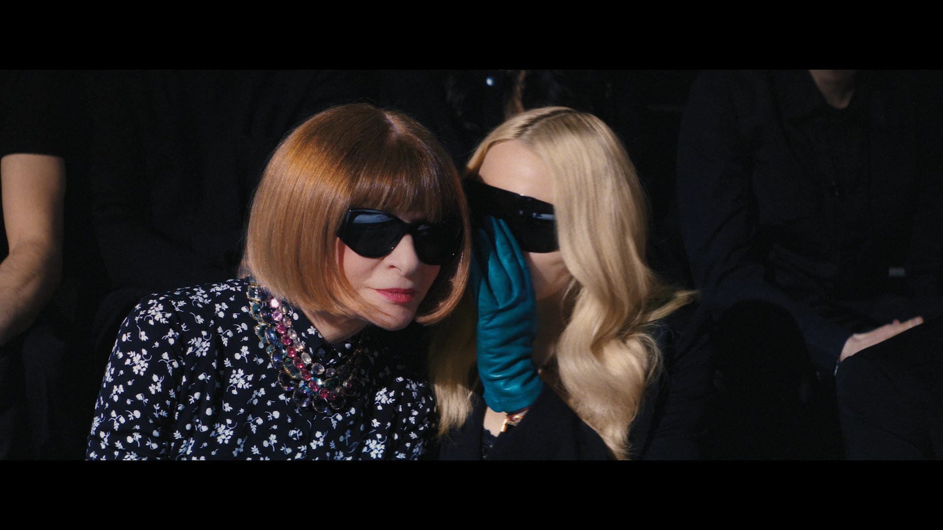 Madonna leans toward Anna Wintour, a blue glove between their faces.
