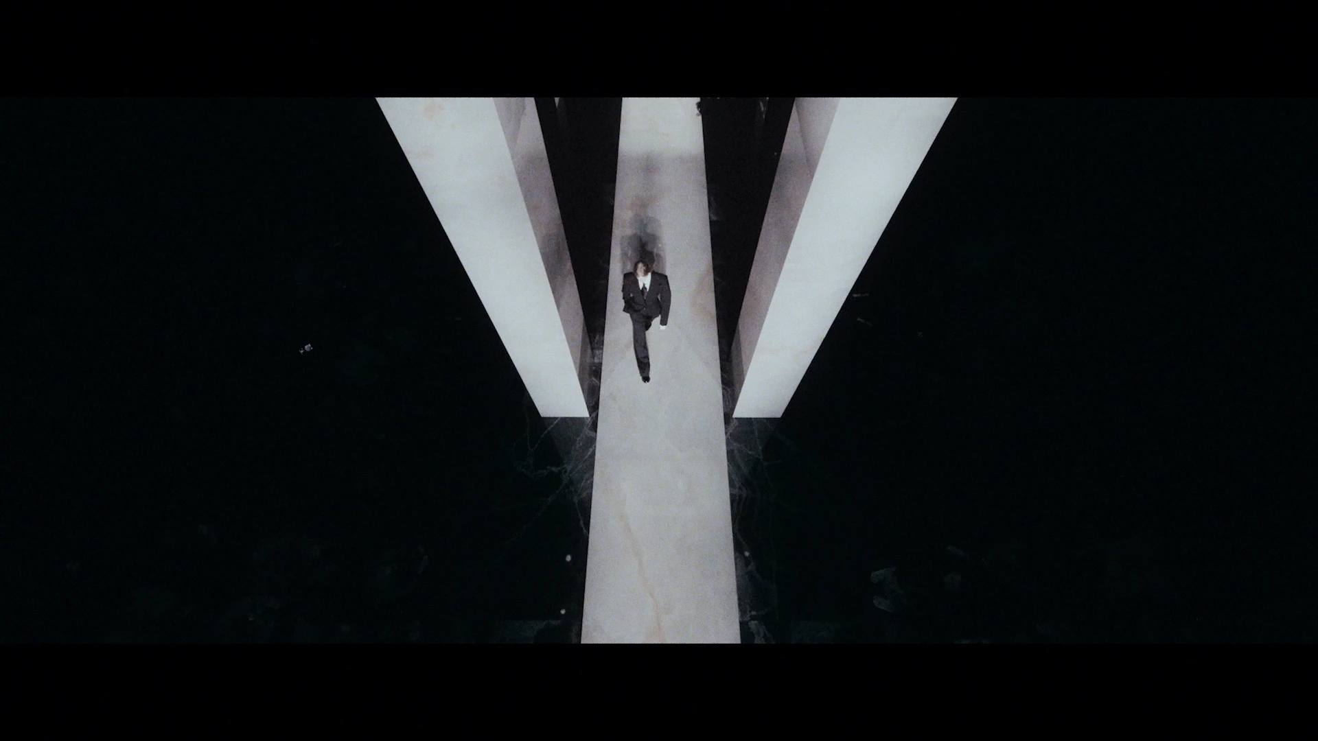 A model walks between white architectural columns, seen from above.