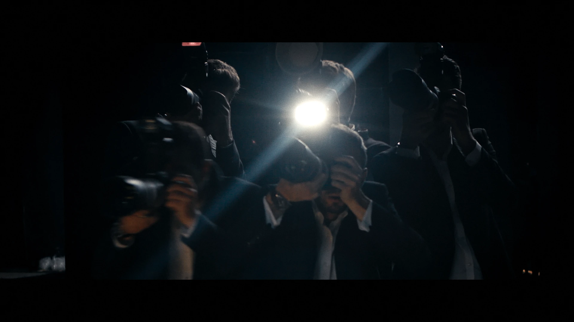 Photographers face the runway in the light of a camera flash.