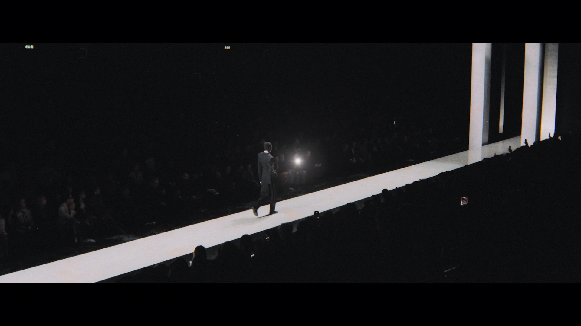 A white runway cuts diagonally through a dark audience.