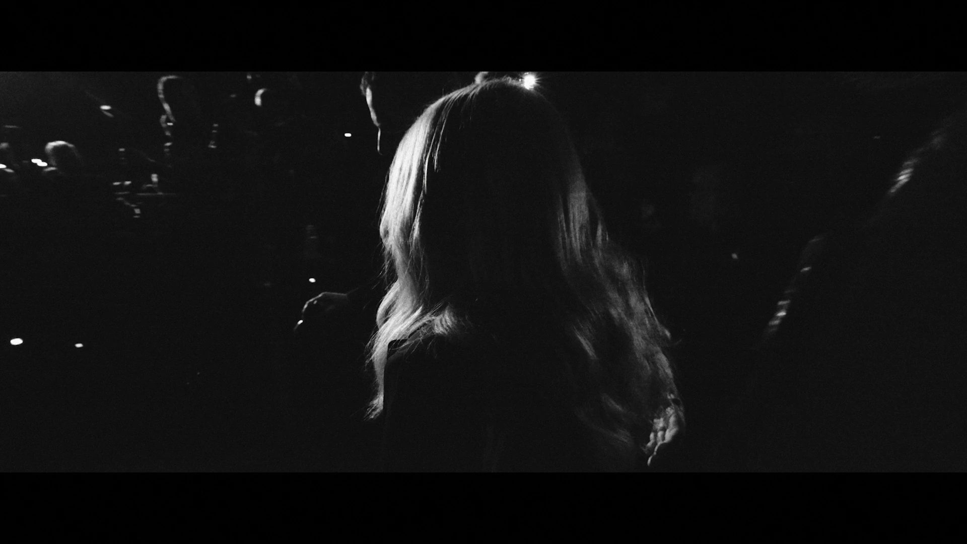 A woman's hair is rim-lit against a dark room.