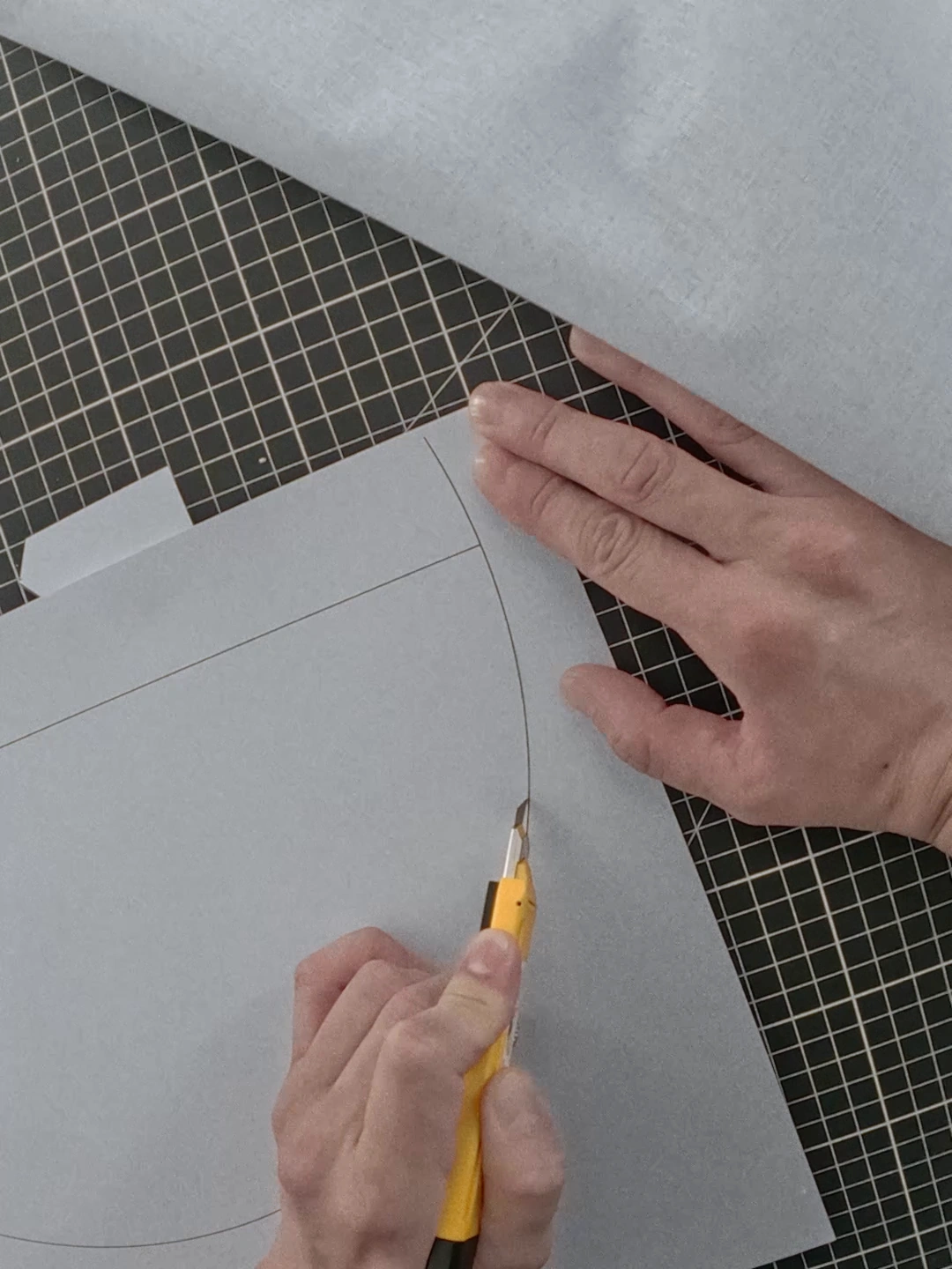 Hands cut a garment pattern on a gridded work surface.