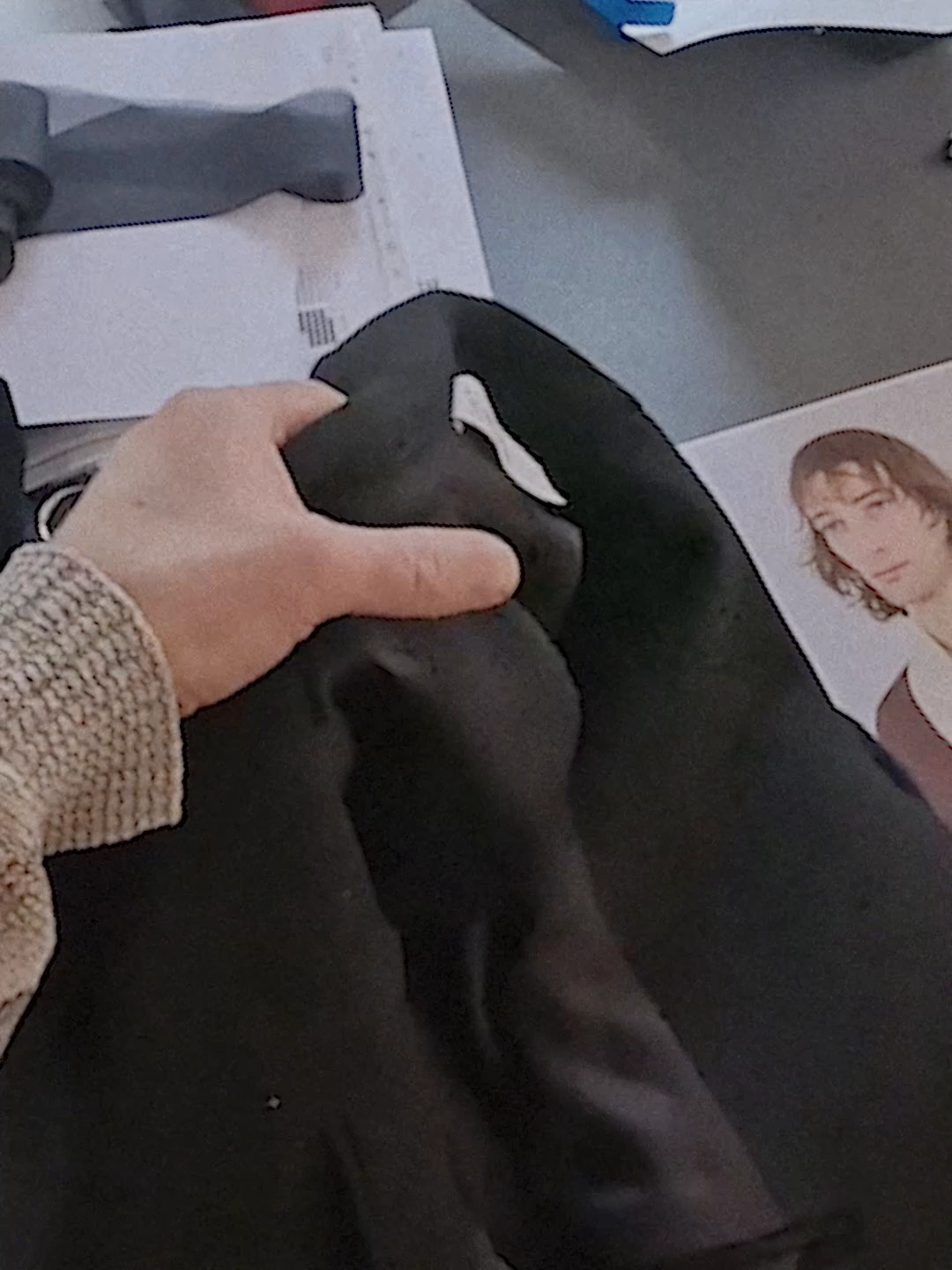 Hands reshape a black garment beside archival imagery.