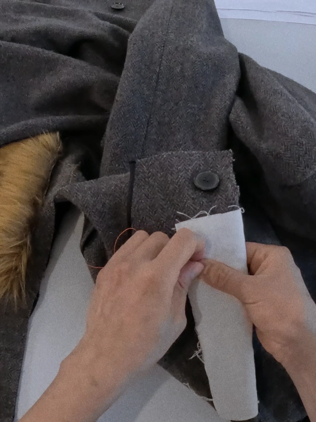 Hands pin a paper pattern to grey tailoring.