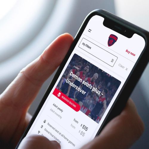 Image of a hand holding an iPhone, on screen is the Melbourne Demons membership website.