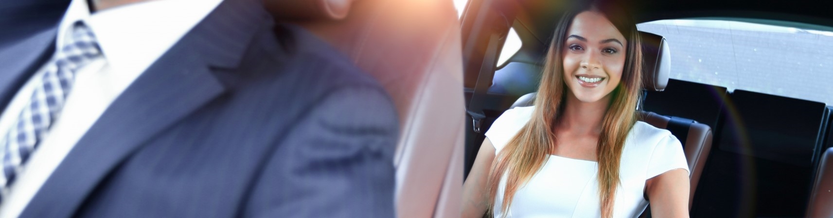 Smiling woman sitting in the back seat of a car with a man in a suit sitting in the front.