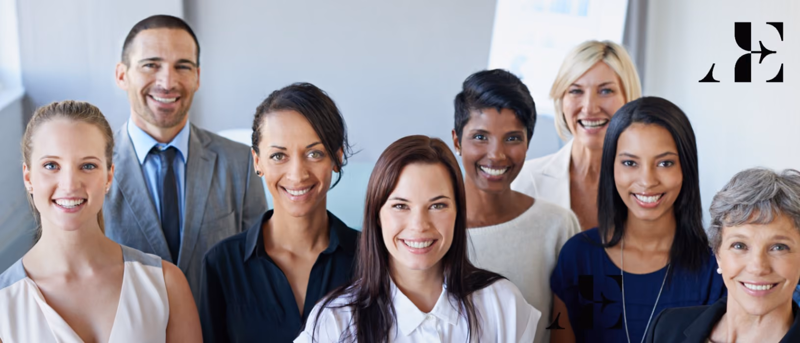 Group of diverse professional men and women smiling and standing close together in a bright office.