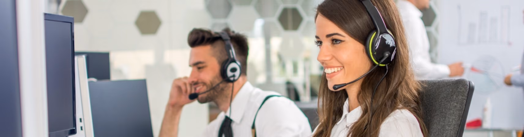 Een lachende vrouw en een man met headsets werken in een modern callcenter.