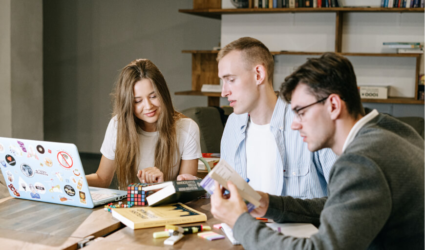 three people sitting at a table looking at a laptop