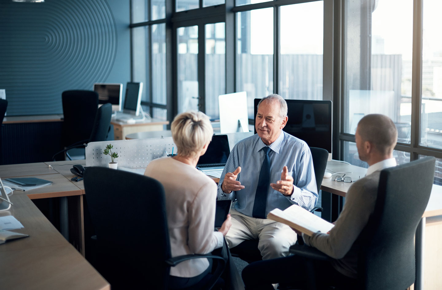 Three professionals having a discussion in a modern office, representing teamwork, business strategy, and professional collaboration in a corporate setting.