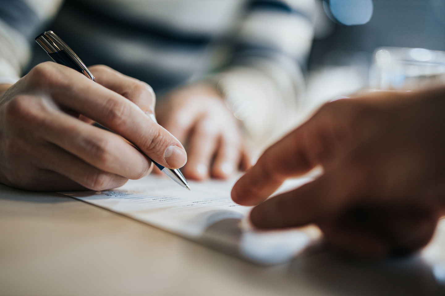 Close-up of a person signing a document with a pen while another hand points, representing legal contract signing, agreement, and professional collaboration.