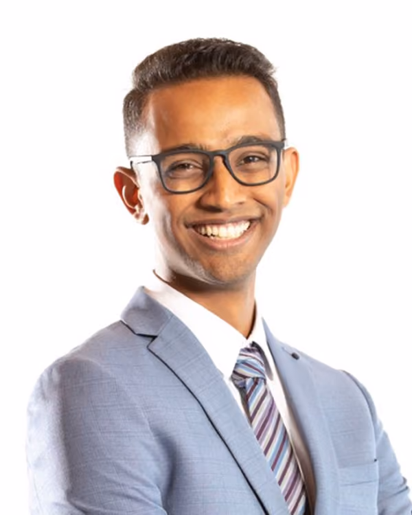 Smiling man wearing glasses, a blue suit, white shirt, and striped tie against a white background.