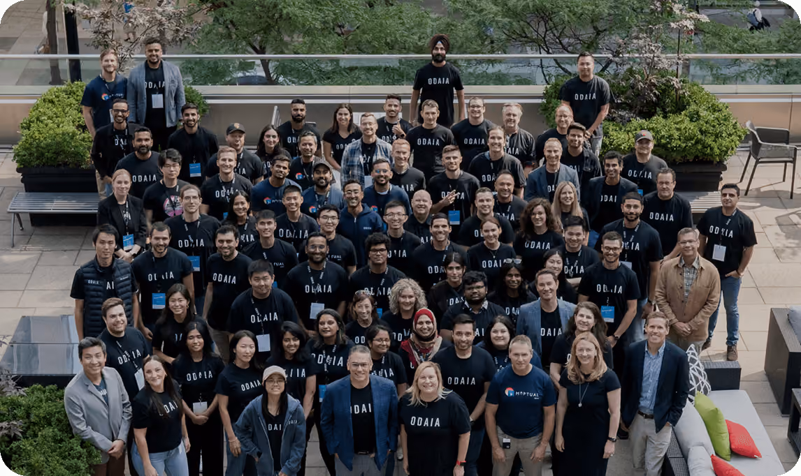 Large group of diverse people gathered outdoors, many wearing ODAIA-branded shirts, posing for a group photo.